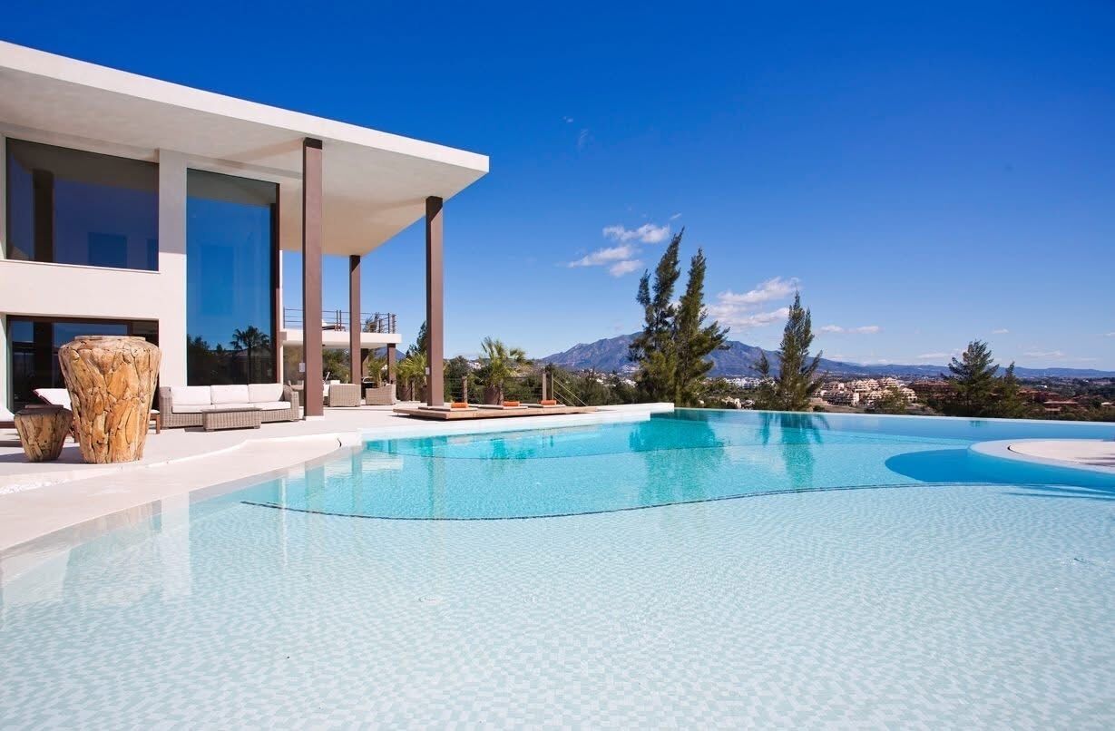 A modern house with a swimming pool, large windows, and a view of mountains.