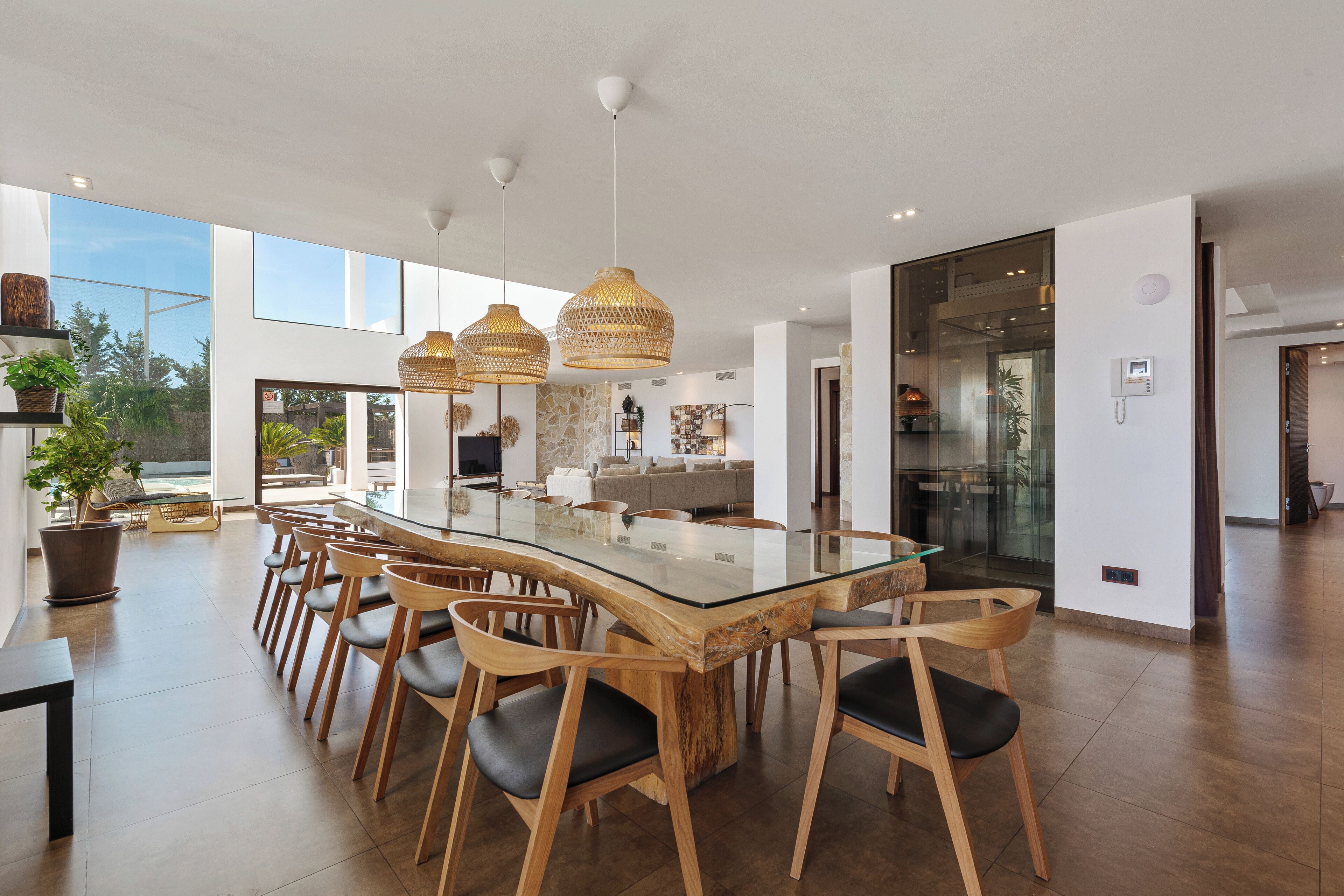 Un comedor amplio con una larga mesa de madera y sillas, lámparas colgantes grandes y vistas al exterior.