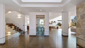 A spacious interior with a central elevator, a staircase on the left, and a stone wall on the right.
