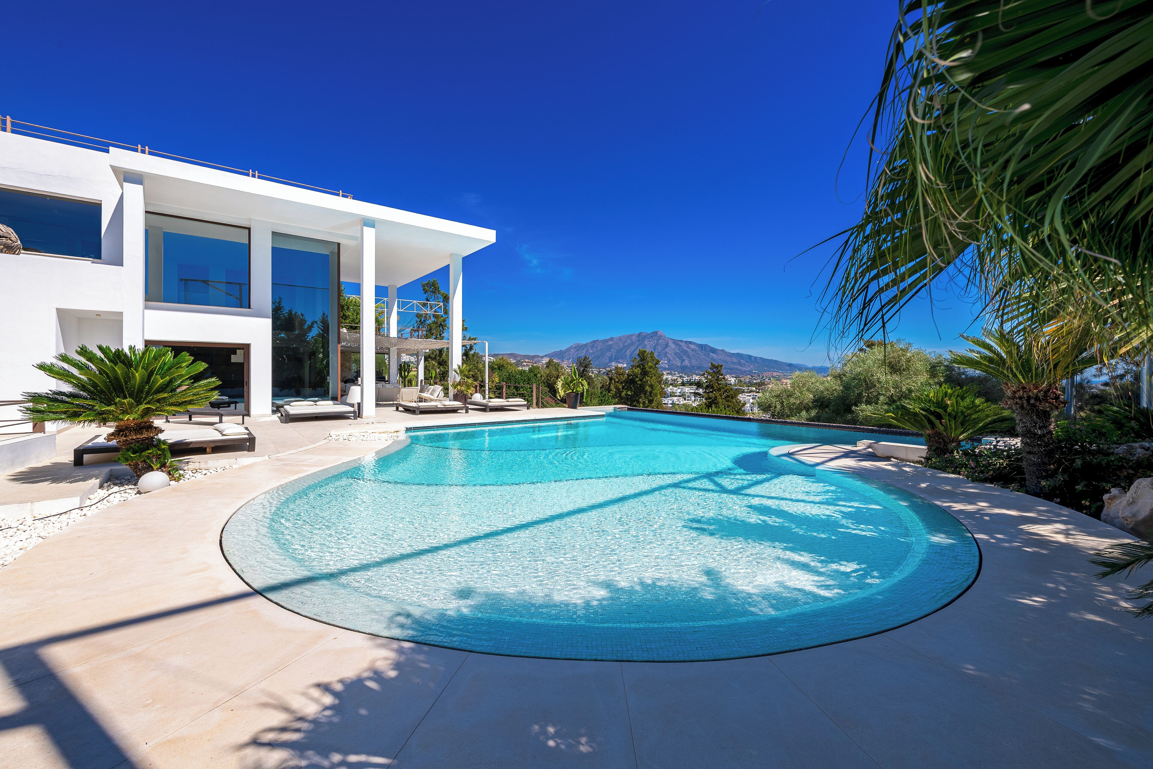 A modern house with a swimming pool, large windows, and a view of mountains.