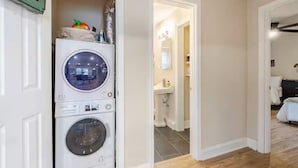 A laundry area with stacked washing machines, a visible bathroom with a sink and mirror, and a hallway leading to another room. - Spacious 3BR Home 10 Mins to Mercedes-Benz Stadium (Atlanta)