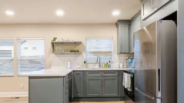 A modern kitchen with grey cabinets, a stainless steel refrigerator, and a window with blinds. - Spacious 3BR Home 10 Mins to Mercedes-Benz Stadium (Atlanta)