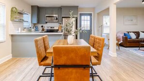 A modern kitchen with grey cabinets, a central island, and a dining area with orange chairs. - Spacious 3BR Home 10 Mins to Mercedes-Benz Stadium (Atlanta)