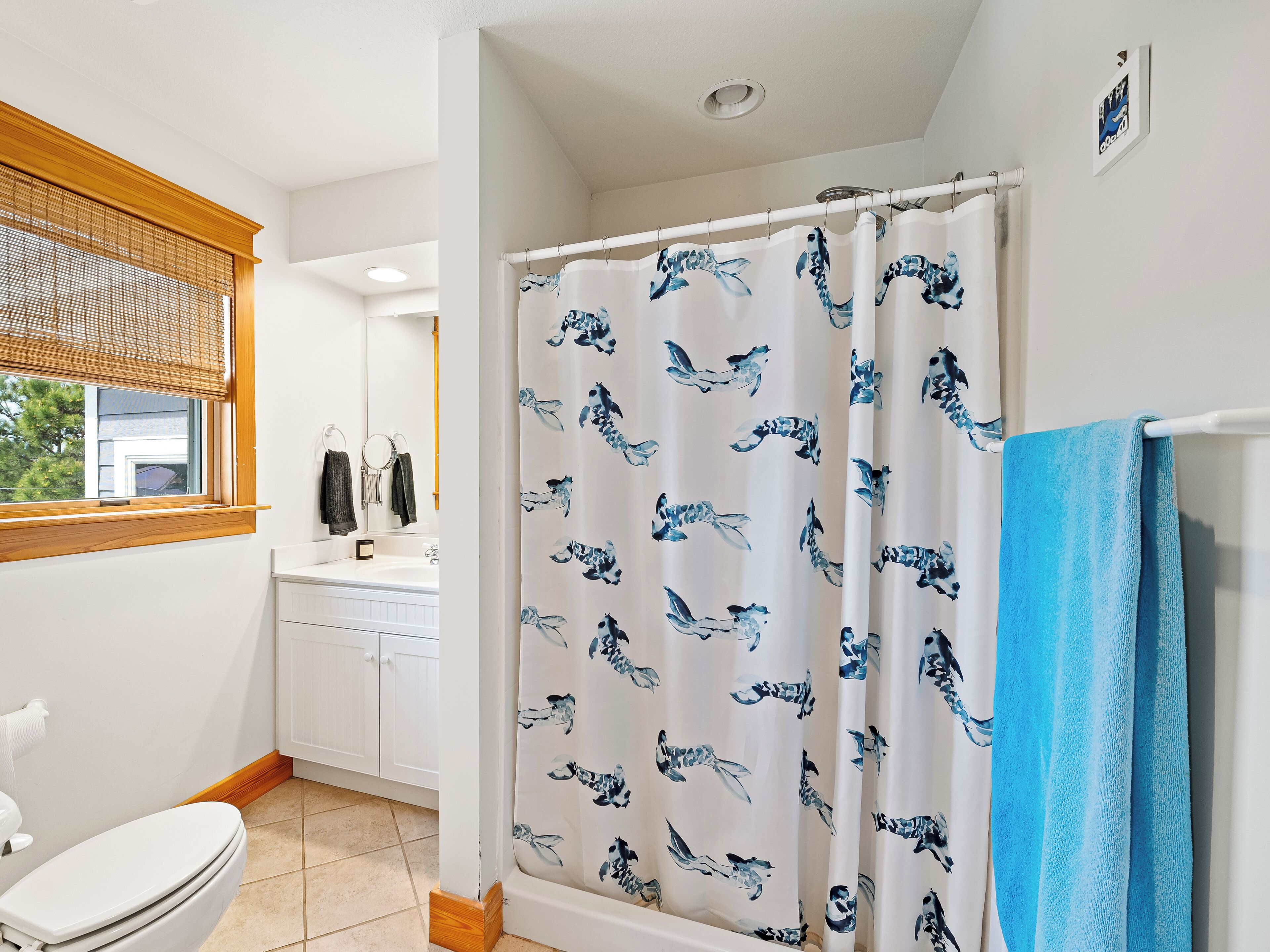 A bathroom with a shower curtain featuring a blue and white pattern, a white toilet, and a window with blinds.