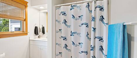A bathroom with a shower curtain featuring a blue and white pattern, a white toilet, and a window with blinds.