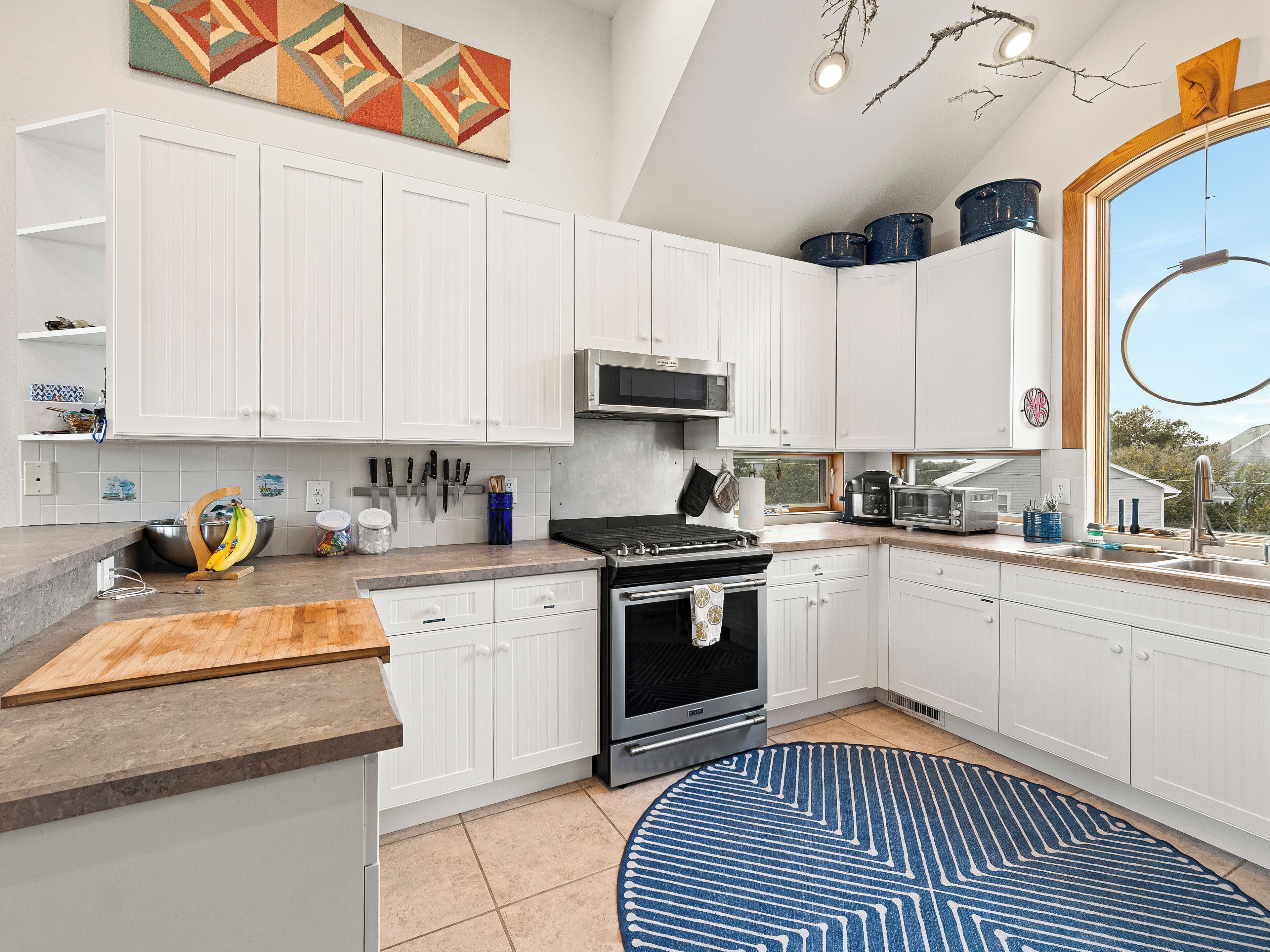 A modern kitchen with white cabinets, a stove, microwave, and a large window.