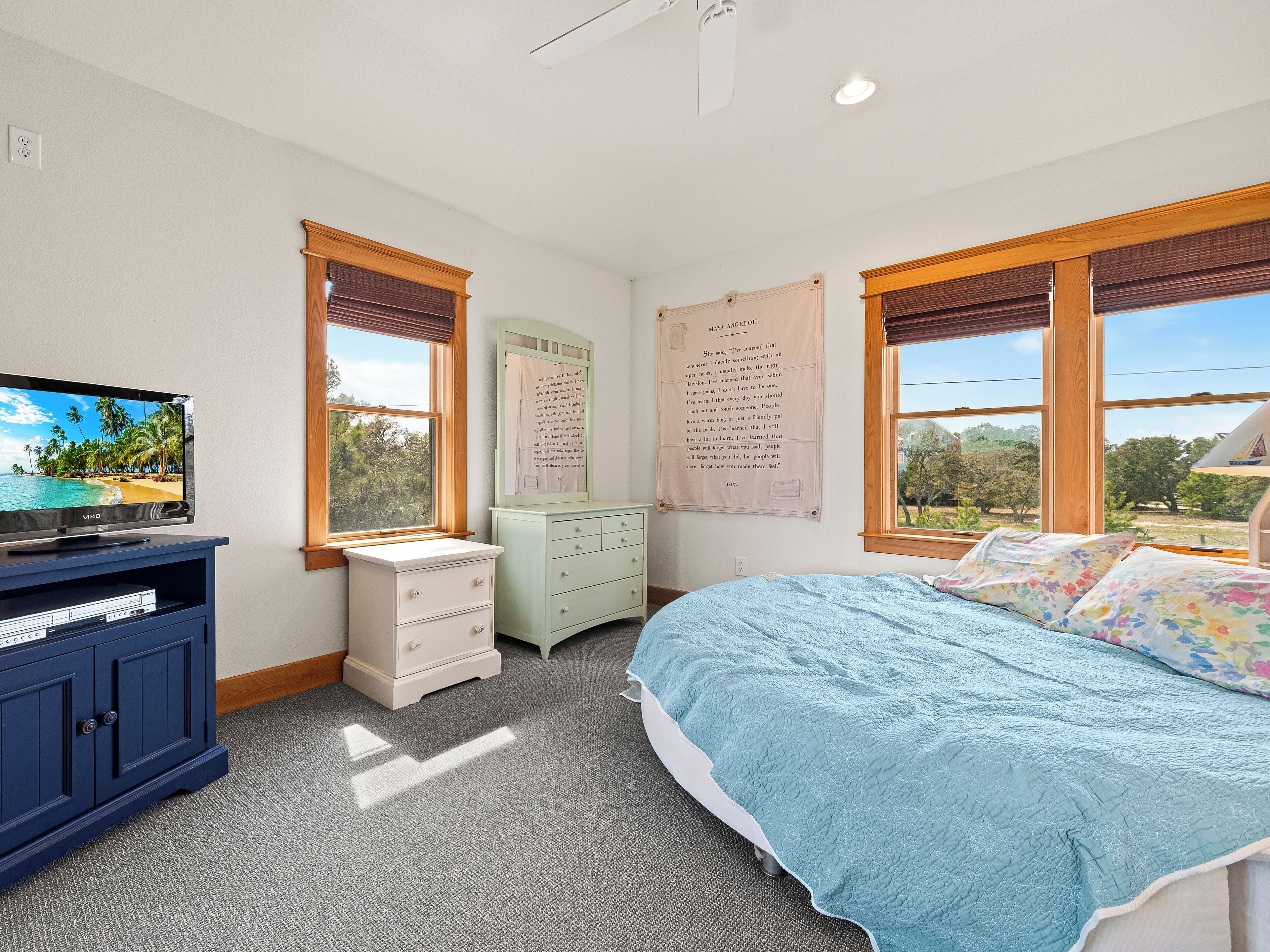 A bedroom with a bed, a dresser, a television, and a window with a view of trees.