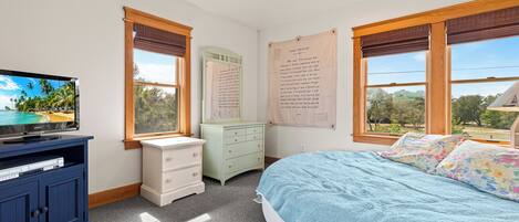 A bedroom with a bed, a dresser, a television, and a window with a view of trees.