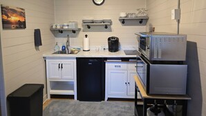 Una cocina compacta con muebles blancos, lavavajillas, cafetera y microondas.