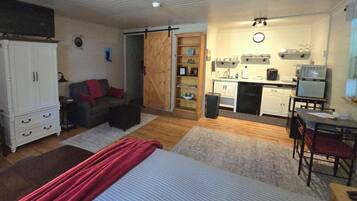 A compact living space with a kitchenette, a bed with a red blanket, a sofa, and a wardrobe.