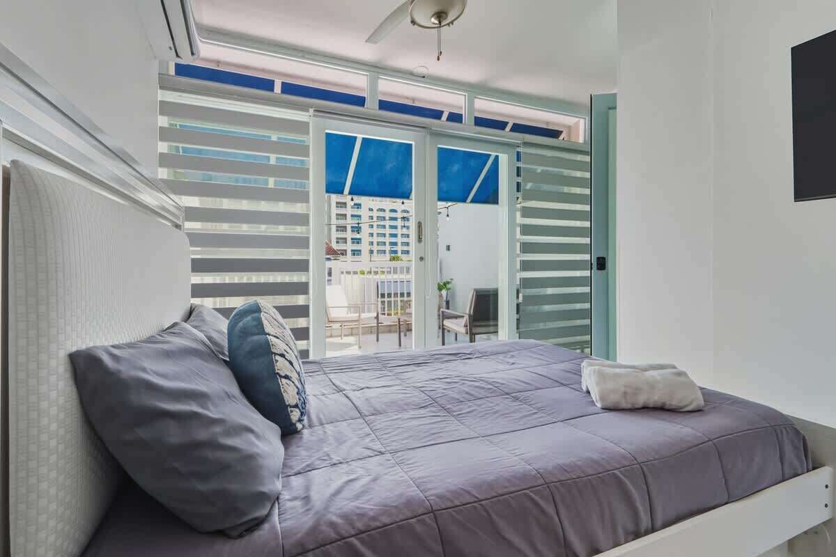 Une chambre à coucher avec un lit, des oreillers, un ventilateur de plafond et une vue sur l’extérieur, accessible par une porte coulissante.