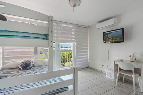 Une chambre avec un lit superposé, un bureau, une chaise, une télévision et une fenêtre avec des stores.