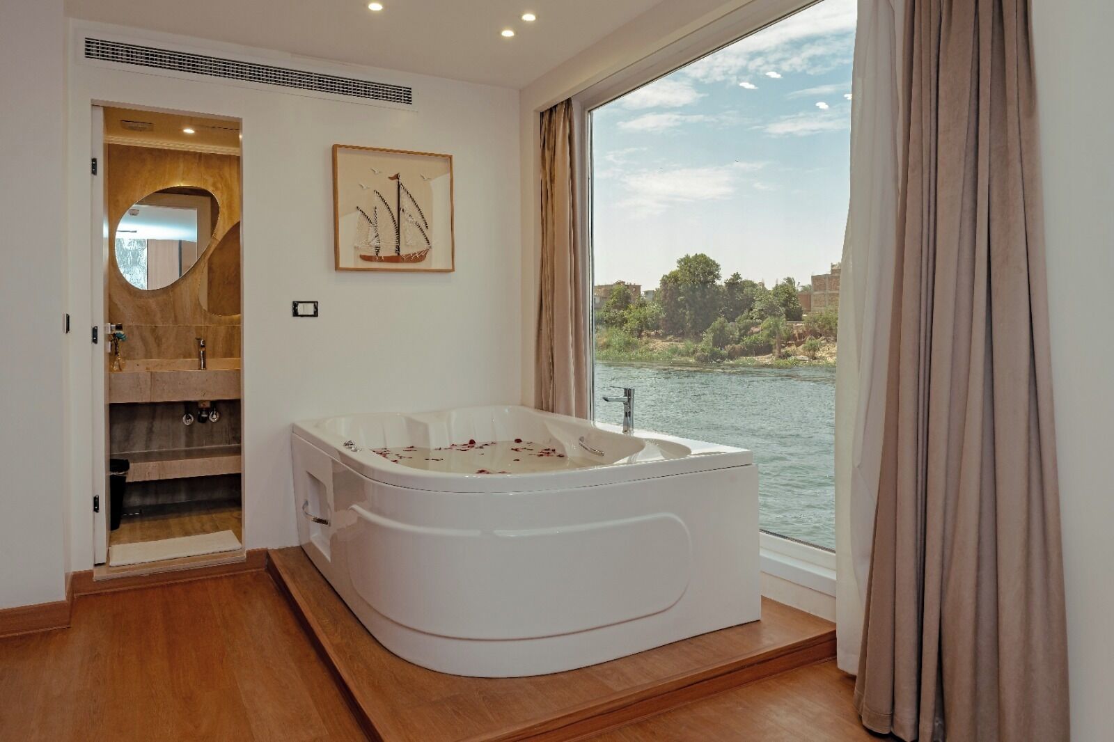 Een moderne badkamer met een ruime badkuip, een houten wastafelmeubel en uitzicht op een rivier.