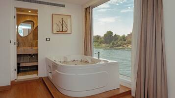 Een moderne badkamer met een ruime badkuip, een houten wastafelmeubel en uitzicht op een rivier.
