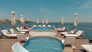 A pool area with lounge chairs and umbrellas, surrounded by water. - Hathor Ultra Luxury Dahabiya Cruise - Saturday from Luxor (Luxor)