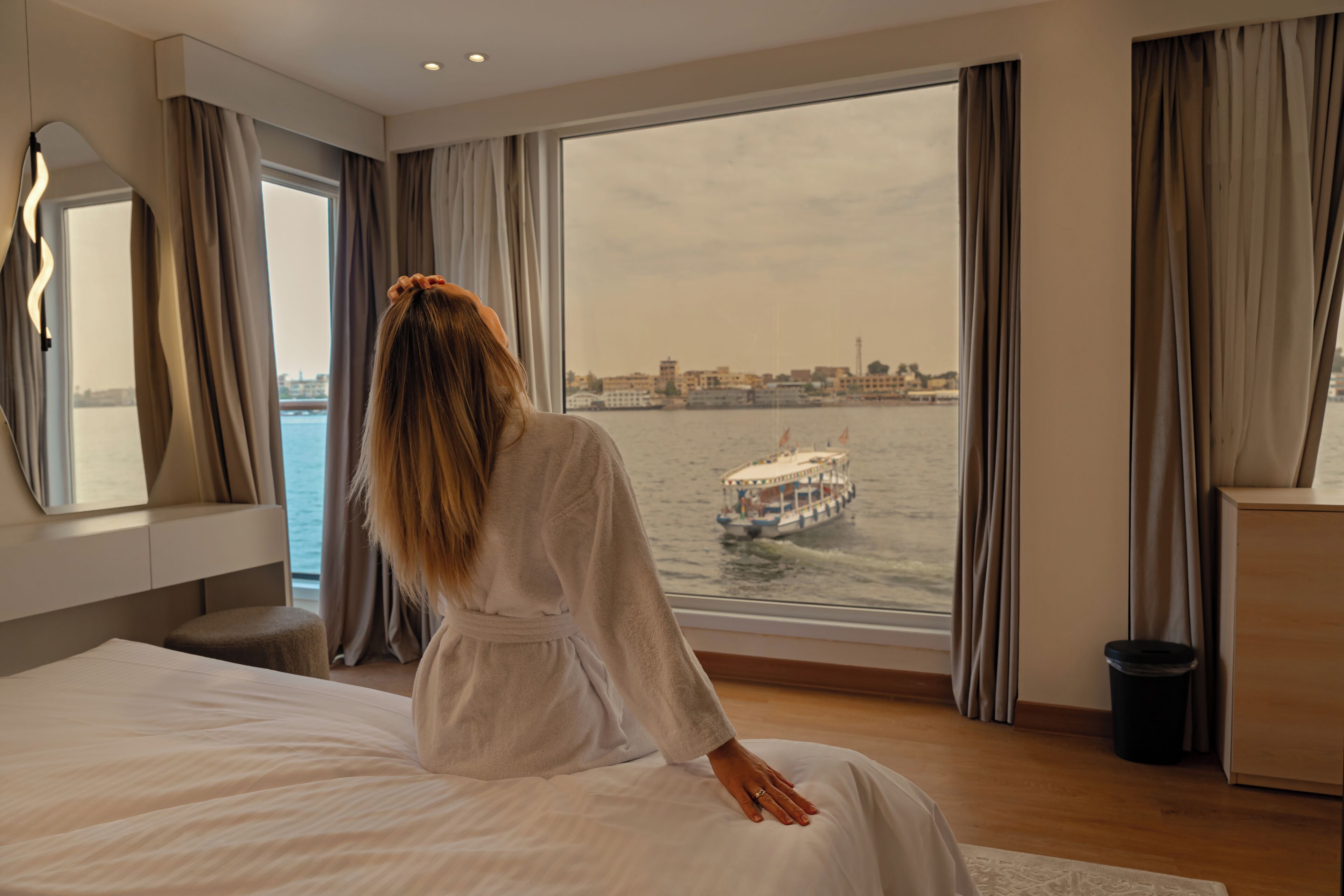 Een hotelkamer met een groot raam, een bed, een nachtkastje en een spiegel.