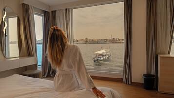 Een hotelkamer met een groot raam, een bed, een nachtkastje en een spiegel.
