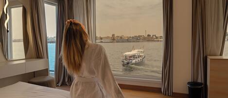A hotel room with a large window, a bed, a nightstand, and a mirror.