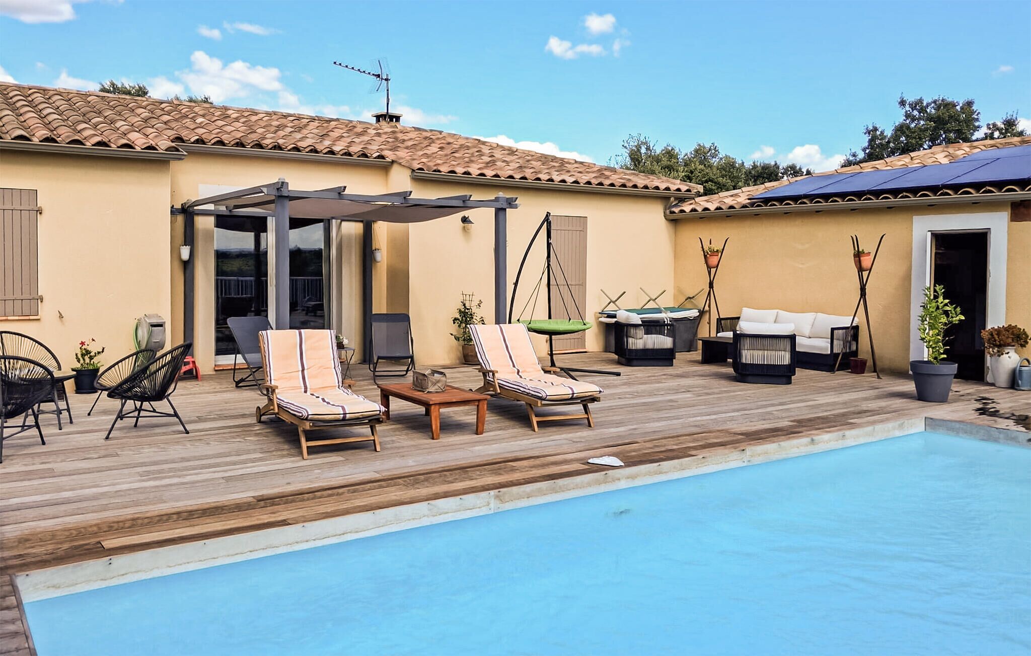 Un espace aménagé au bord de la piscine, avec des chaises longues, une pergola et une petite table.