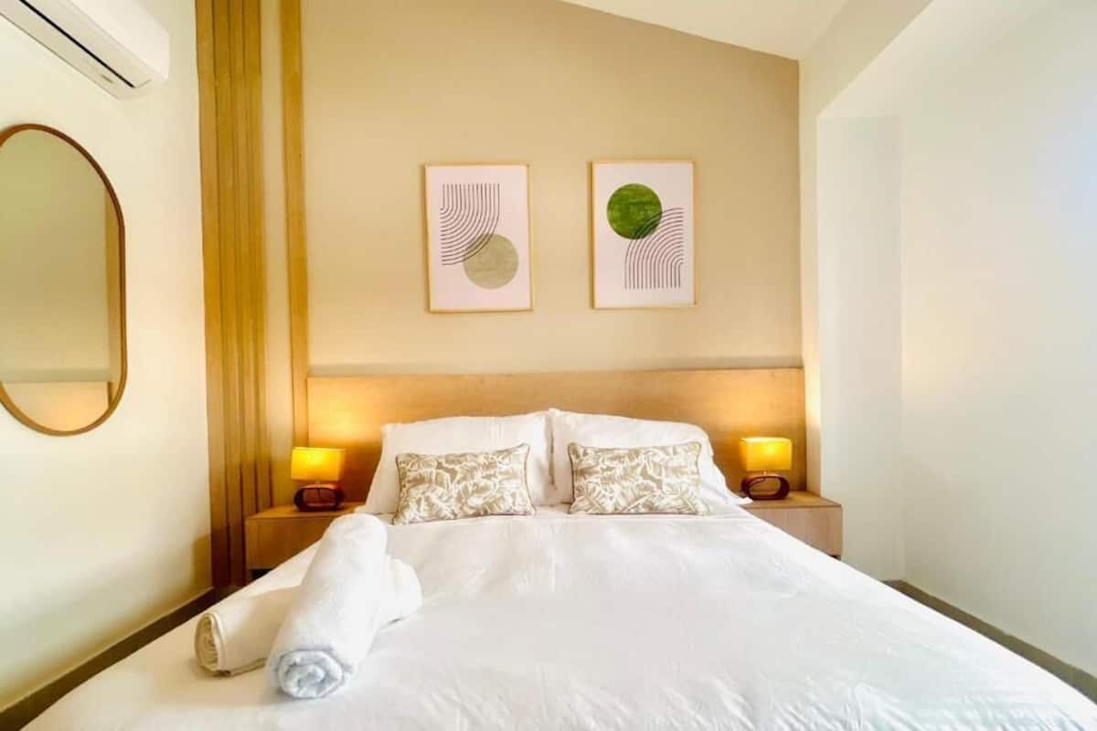 A hotel room with a neatly made bed, two bedside lamps, and two framed artworks on the wall.