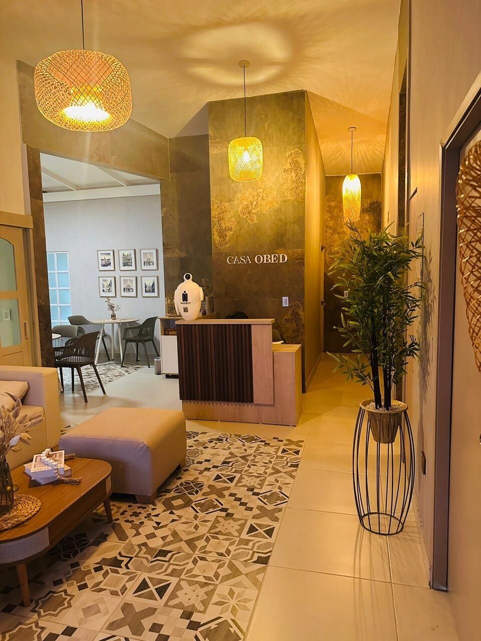 Uma área de recepção com balcão, espaço de estar com sofá e cadeiras, piso estampado e luminárias pendentes.