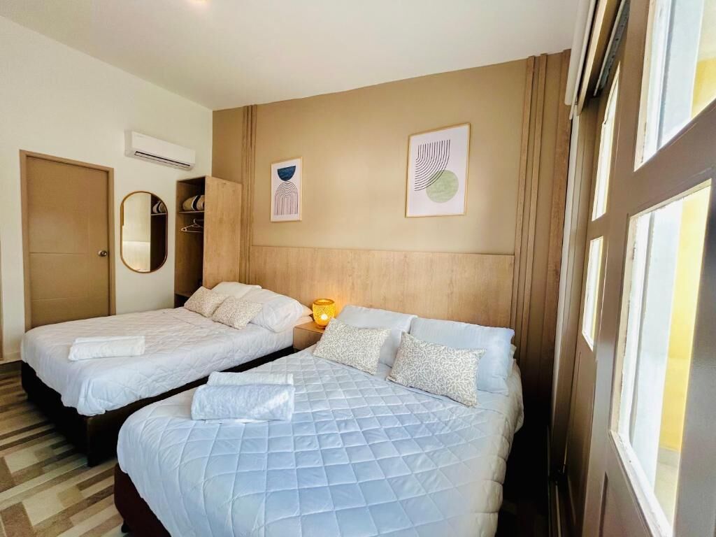 A hotel room with two beds, a mirror, a wardrobe, and artwork on the wall.