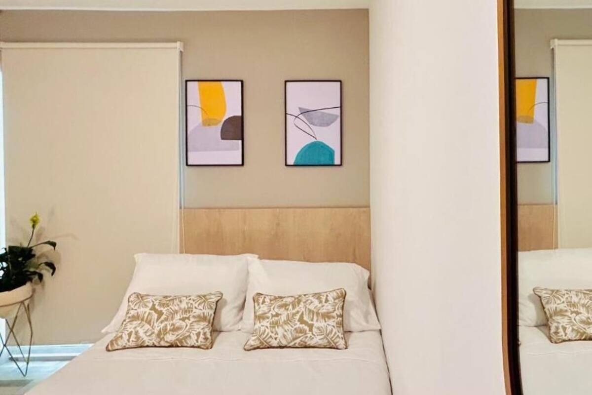 A bedroom with a bed, pillows, and two abstract paintings on the wall.
