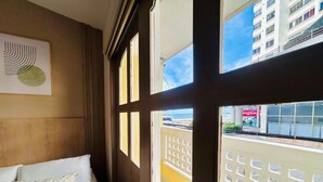 Ein Hotelzimmer mit einem Bett, einem Fenster mit Blick nach draußen und einem an der Wand hängenden Kunstwerk.