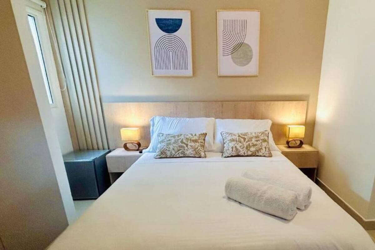 A hotel room with a large bed, two bedside tables with lamps, and two abstract wall art pieces.