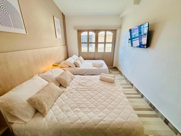 A hotel room with two beds, a TV on the wall, and a window with a view. - HOTEL CASA OBED (Cartagena)