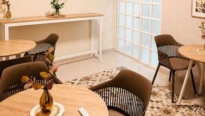 Ein modernes Zimmer mit rundem Tisch, Stühlen, einem kleinen Schreibtisch und einem Fenster mit Jalousien.