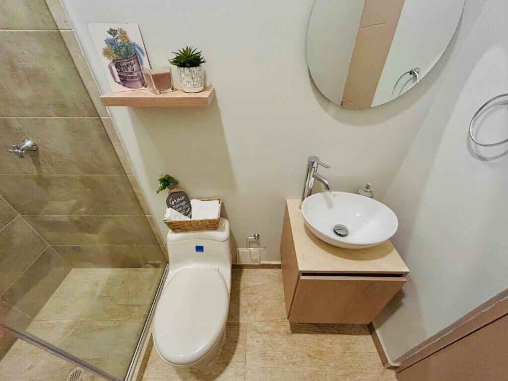 Une salle de bain moderne équipée de toilettes, d’un lavabo et d’une douche. On peut voir des objets décoratifs sur une étagère située au-dessus des toilettes.