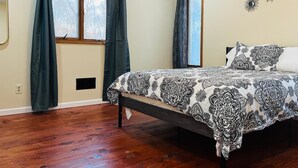 A bedroom with a wooden floor, a bed with a patterned bedspread, two windows with curtains, and wall-mounted decorative elements. - Spacious Camelback Retreat w/ Fireplace (Henryville)