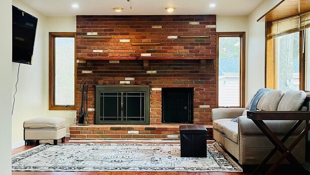 A living room with a brick fireplace, wooden flooring, a ceiling fan, and a sofa. - Spacious Camelback Retreat w/ Fireplace (Henryville)