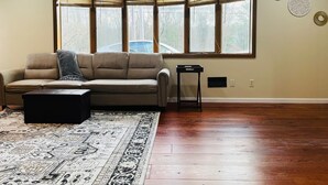 A living room with a beige sofa, a black ottoman, and a patterned rug. - Spacious Camelback Retreat w/ Fireplace (Henryville)