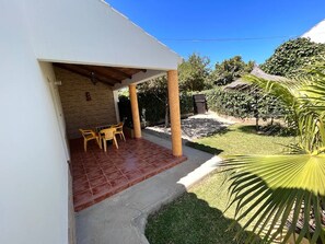 Un patio cubierto con una mesa y sillas, un muro de ladrillo y un jardín con una palmera.
