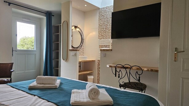 A hotel room with a bed, a TV mounted on the wall, a bathroom with a shower, and a chair. - Bed and Breakfast Île d'Hoëdic (BELZ)