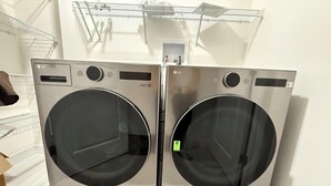 Un par de lavadoras LG de carga frontal en una sala de exposición, con suelo de baldosas blancas y estanterías metálicas al fondo.