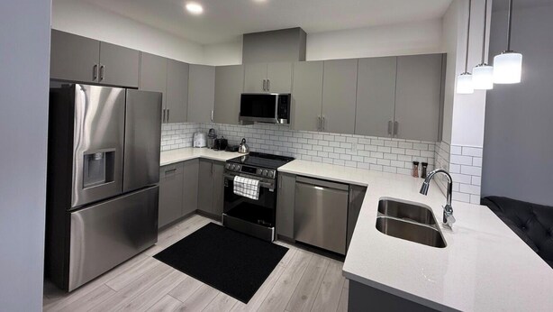 Una cocina moderna con electrodomésticos de acero inoxidable, salpicadero de azulejos blancos y alfombra negra.