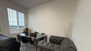 Una sala de estar moderna con comedor, que incluye un sofá de cuero, una mesa de comedor con sillas y un gran ventanal con persianas.