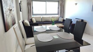 Un espace repas moderne avec une table à plateau en verre, des chaises noires et un canapé en arrière-plan.