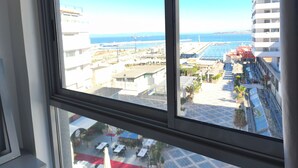 Une vue depuis une fenêtre donnant sur une zone côtière, avec des bâtiments, une piscine et un ciel dégagé.