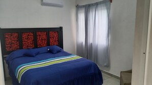 Une chambre à coucher avec un lit, une tête de lit à motifs rouges et noirs, et une fenêtre avec des rideaux gris.
