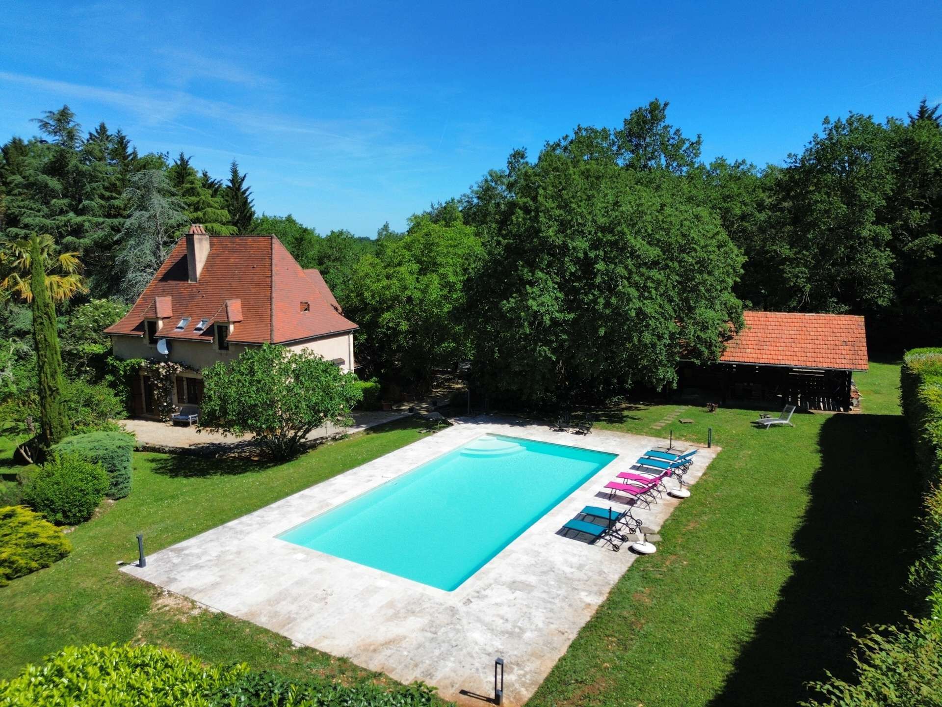 En swimmingpool med solstolar, ett hus och omgivande grönska.