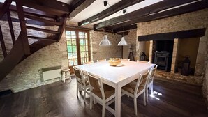 A rustic dining room with a wooden table, white chairs, and a stone wall. - Le Tuquet de Saint Chamassy, private swimming pool (ST CHAMASSY)
