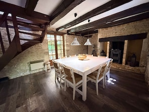 Ein rustikaler Essraum mit Holztisch, weißen Stühlen und einer Steinwand.