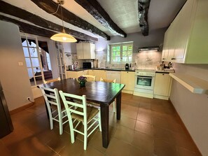 A kitchen with a wooden table, white chairs, a window, and a stove. - Le Tuquet de Saint Chamassy, private swimming pool (ST CHAMASSY)