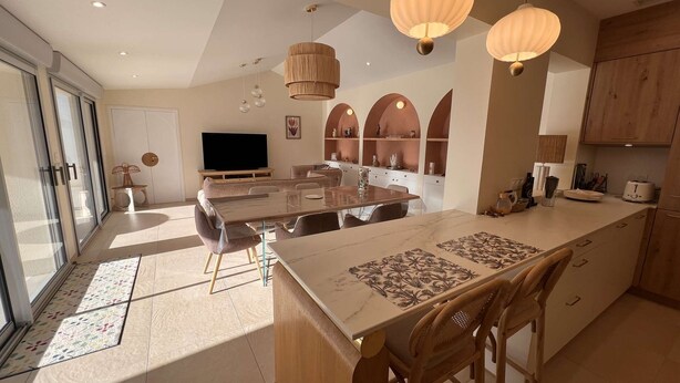 A modern kitchen with a large island, pendant lights, and a dining area with a TV. - Ref 038 - Exceptional villa with private pool and jacuzzi in the center of Soulac-sur-Mer (SOULAC SUR MER)