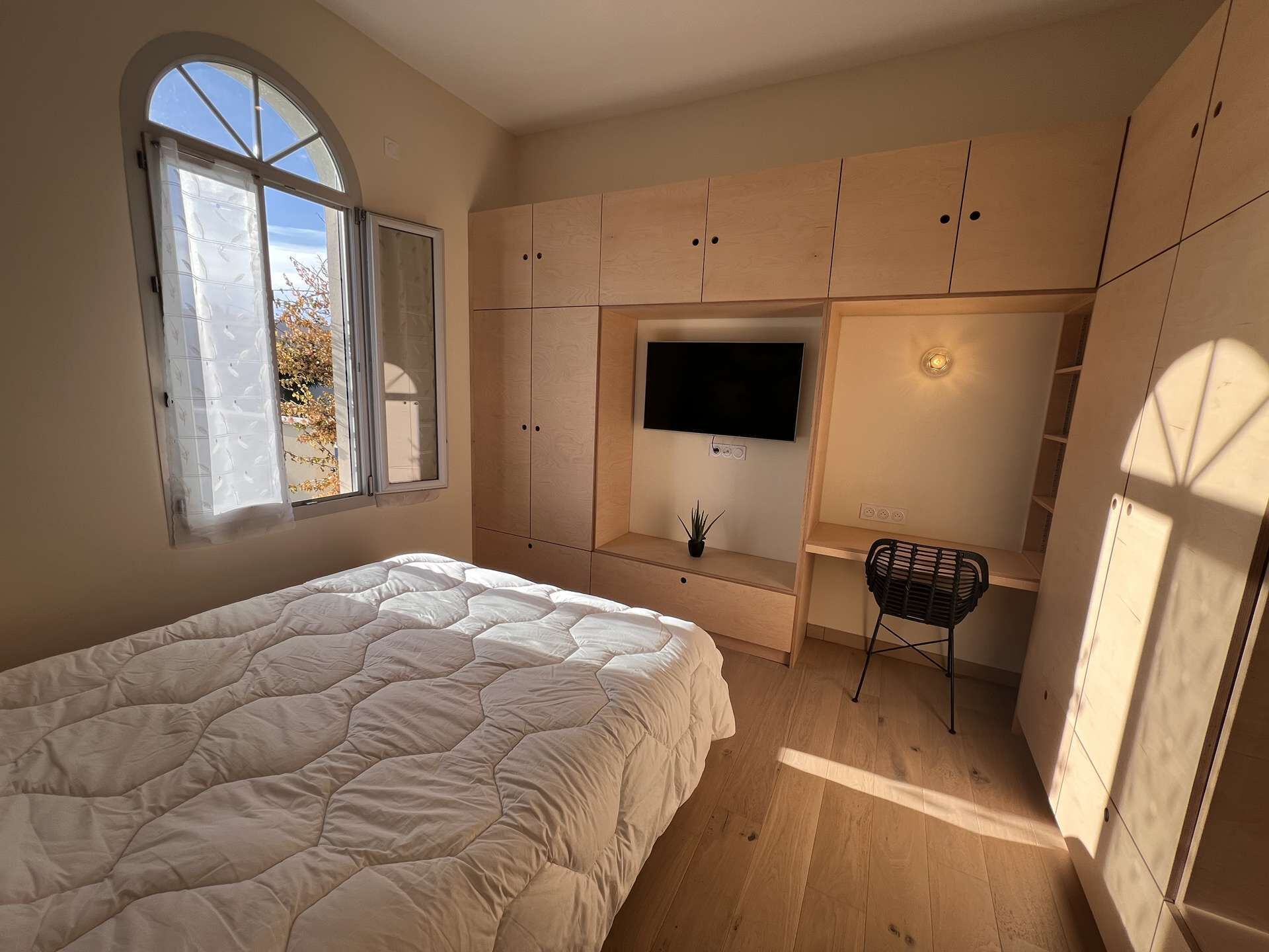 A bedroom with a bed, a TV, and built-in wooden storage.