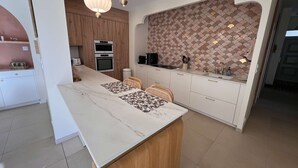 A modern kitchen with a marble countertop, wooden cabinets, and a tiled backsplash. - Ref 038 - Exceptional villa with private pool and jacuzzi in the center of Soulac-sur-Mer (SOULAC SUR MER)